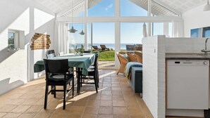 Cocina y comedor de planta libre y luminosa, con amplios ventanales, pared de ladrillo y vista al mar.