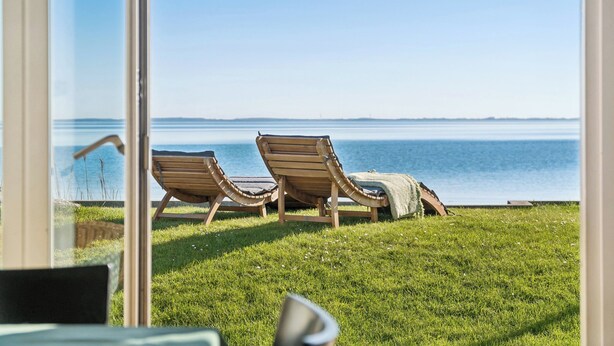 Vista de un área verde con dos sillones de madera mirando un cuerpo de agua.