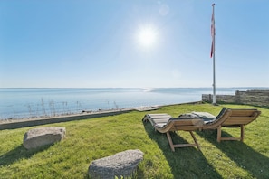 A grassy area with two lounge chairs facing a body of water, a flagpole, and a clear sky. - Two holiday homes – perfect for holiday together (Svendborg)