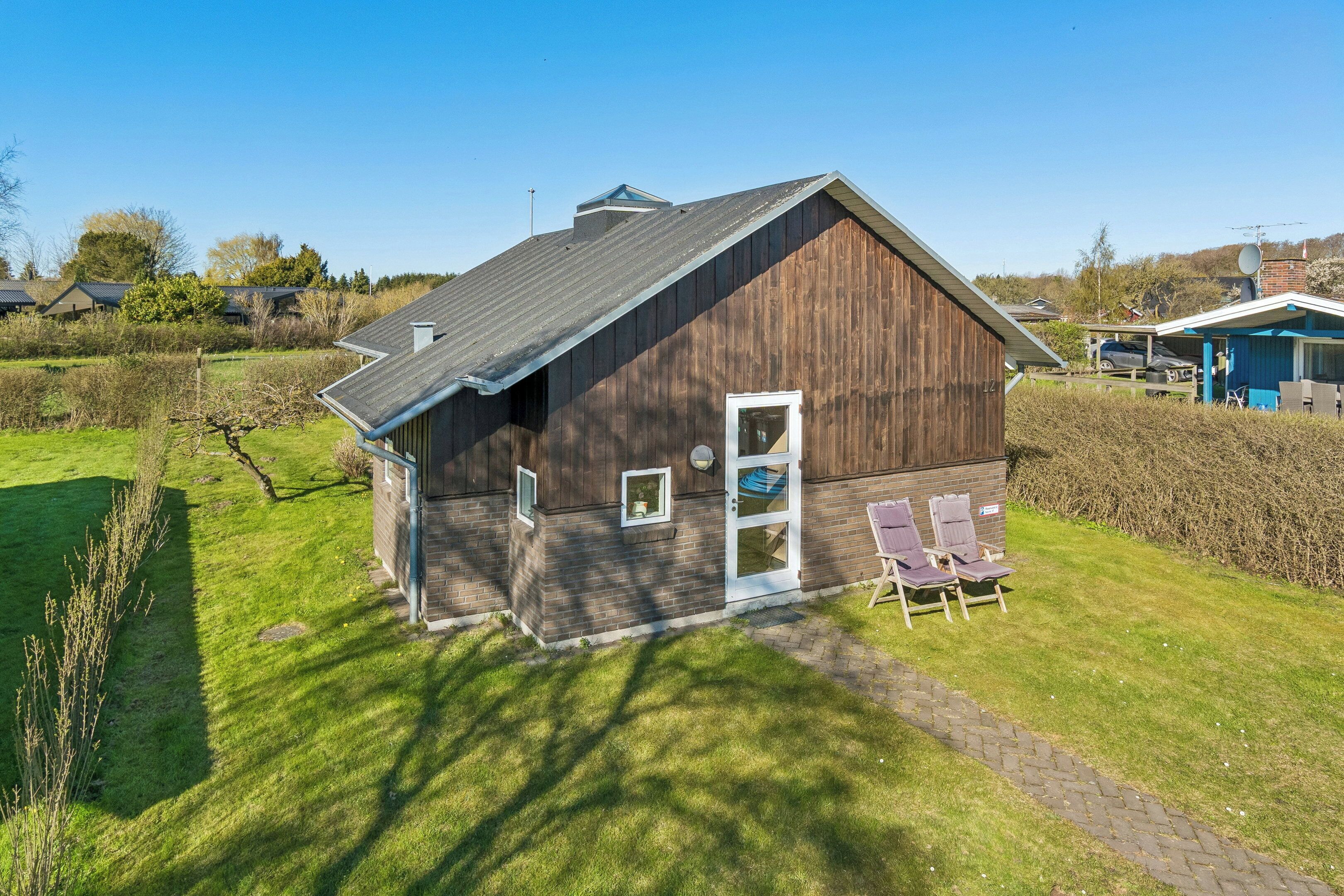 A single-story building with a sloped roof, a door, and a small porch area with two chairs.