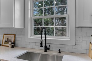 A kitchen with a stainless steel sink, a window with a view of trees, and a framed picture on the counter. - Sleep 9 Boiling Springs SC w/2 kings, Pool Table (Boiling Springs)