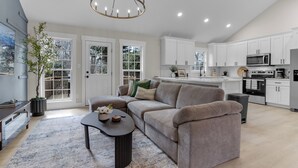 A modern kitchen with white cabinets, a central island, and a dining area with a dark-colored sofa and a coffee table. - Sleep 9 Boiling Springs SC w/2 kings, Pool Table (Boiling Springs)