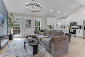 A modern kitchen with white cabinets, a central island, and a dining area with a dark-colored sofa and a coffee table. - Sleep 9 Boiling Springs SC w/2 kings, Pool Table (Boiling Springs)