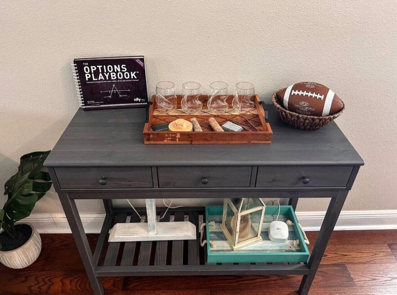 Un escritorio de madera oscura con un atril de vasos, un balón de fútbol y un libro titulado 'The Options Playbook'.