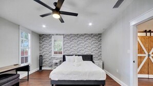 A bedroom with a bed, a desk, a chair, a ceiling fan, a window, and a brick-patterned wall. - Spacious Getaway | Cozy & Modern | Backyard Dream (Tampa)