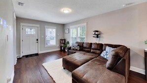 A living room with a sectional sofa, a white rug, and a bookshelf. - Spacious Getaway | Cozy & Modern | Backyard Dream (Tampa)