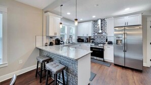 A modern kitchen with a central island, stainless steel appliances, and a patterned backsplash. - Spacious Getaway | Cozy & Modern | Backyard Dream (Tampa)