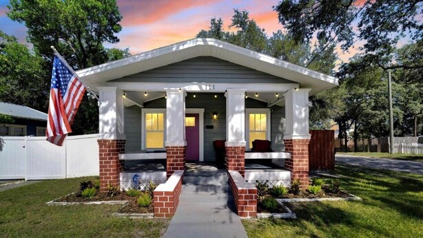 A single-story house with a covered porch, a flag, and a well-maintained lawn. - Spacious Getaway | Cozy & Modern | Backyard Dream (Tampa)