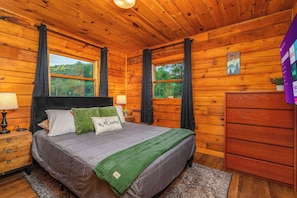 Ein Schlafzimmer einer Holzhütte mit Bett, Nachttisch, Kommode und Fenstern.