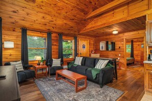 Ein rustikales Holzhaus-Interieur mit einer Couch, einem Holztisch, einer Lampe und Blick ins Freie.