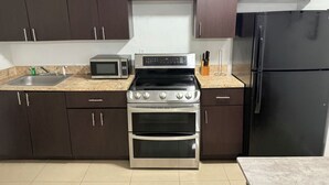 Una cocina con armarios marrón oscuro, una estufa de acero inoxidable, un microondas y un refrigerador negro.