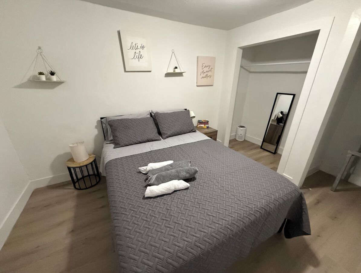 Une chambre à coucher avec un lit, des oreillers, une table de chevet, une petite étagère avec des plantes et des œuvres d’art mural.