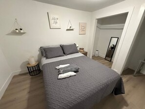 A bedroom with a bed, pillows, a bedside table, a small shelf with plants, and wall art. - Miami Central Rest Pad for 2 (Miami)