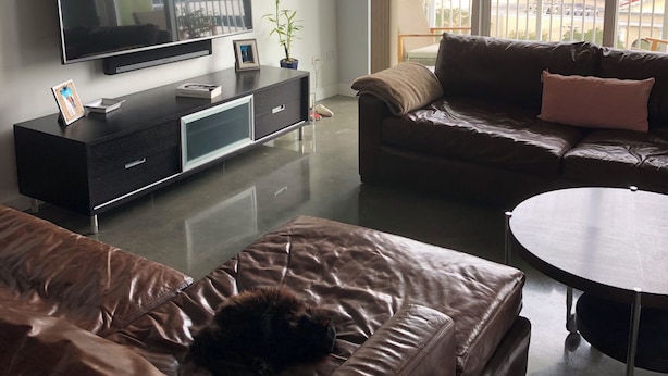 Un soggiorno moderno con una televisione a schermo piatto, divani in pelle, un piccolo tavolino rotondo e un'ampia finestra con vista sulla città.