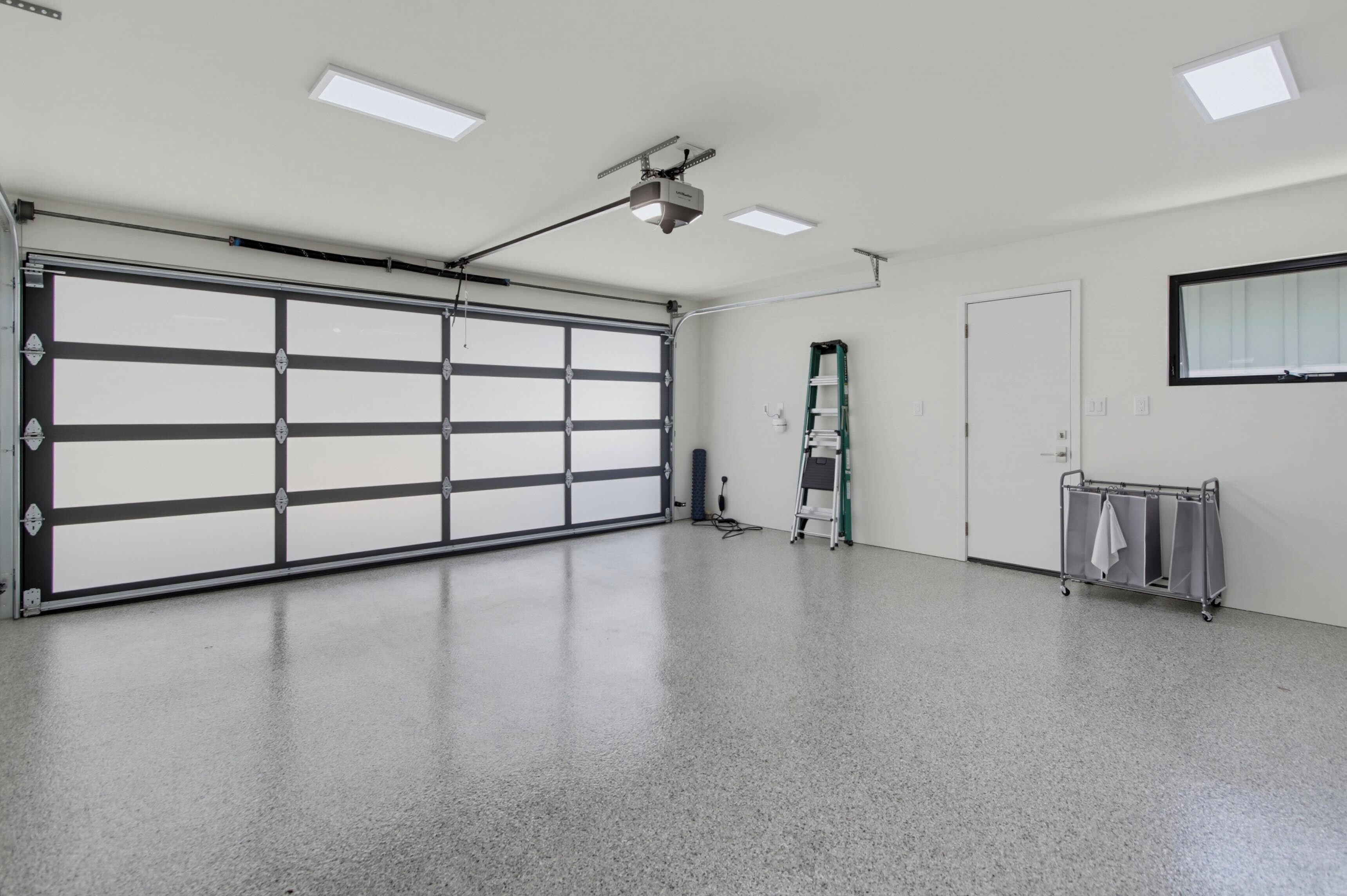Un garage spacieux doté d’une grande porte de garage, de luminaires fixés au plafond, d’une échelle et d’un chariot utilitaire.