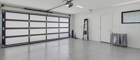 Un garage spacieux doté d’une grande porte de garage, de luminaires fixés au plafond, d’une échelle et d’un chariot utilitaire.