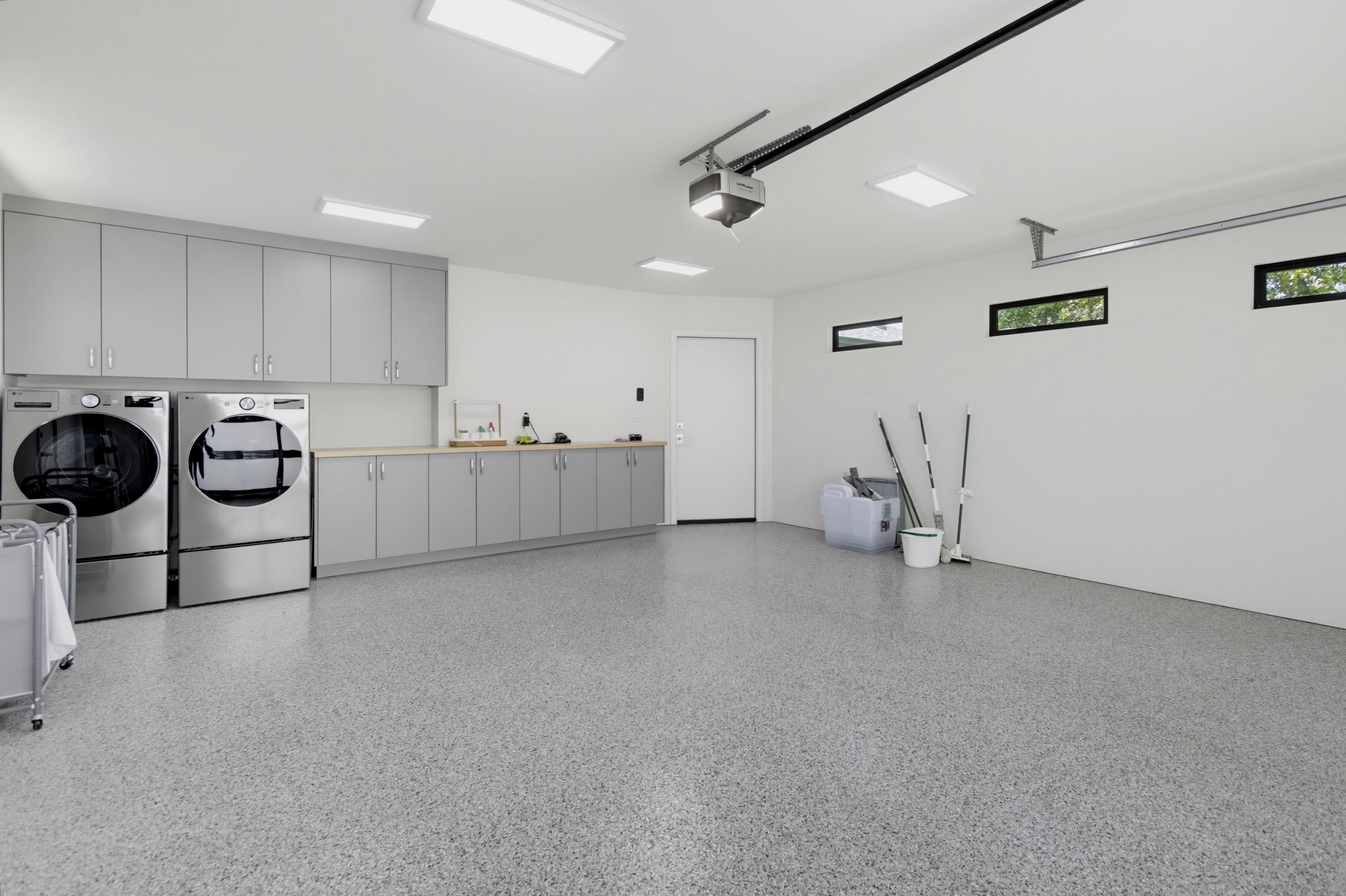 A modern kitchen with stainless steel appliances, grey cabinets, and a grey speckled floor.