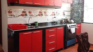 Een keuken met rode kastjes, een zwart aanrecht, een fornuis en een raam met een stenen muur.