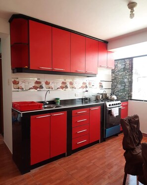A kitchen with red cabinets, a black countertop, a stove, and a window with a stone wall. - Family Department (cuzco)