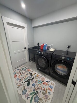 A laundry room with a washing machine, dryer, and a small countertop with cleaning supplies. - Remodeled Cape Coral Retreat with Pool, Massive Kitchen, & Entertainment Space (Cape Coral)