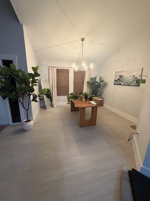 Ein Essbereich mit Tisch, Stühlen, Zimmerpflanzen, einem Chandelier und einem Gemälde an der Wand.