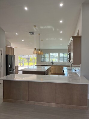 A modern kitchen with a large island, pendant lighting, and a view to the outdoors. - Remodeled Cape Coral Retreat with Pool, Massive Kitchen, & Entertainment Space (Cape Coral)