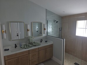 Un baño moderno con cabina de ducha de vidrio, un lavamanos doble con dos espejos, y un ventanal que proporciona luz natural.
