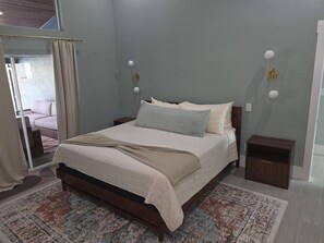 Un dormitorio con cama, mesitas de noche, alfombra y vistas a un balcón.