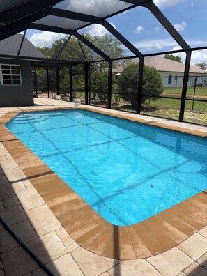 A clear swimming pool with a tiled deck, surrounded by a covered area with a metal frame. - Remodeled Cape Coral Retreat with Pool, Massive Kitchen, & Entertainment Space (Cape Coral)