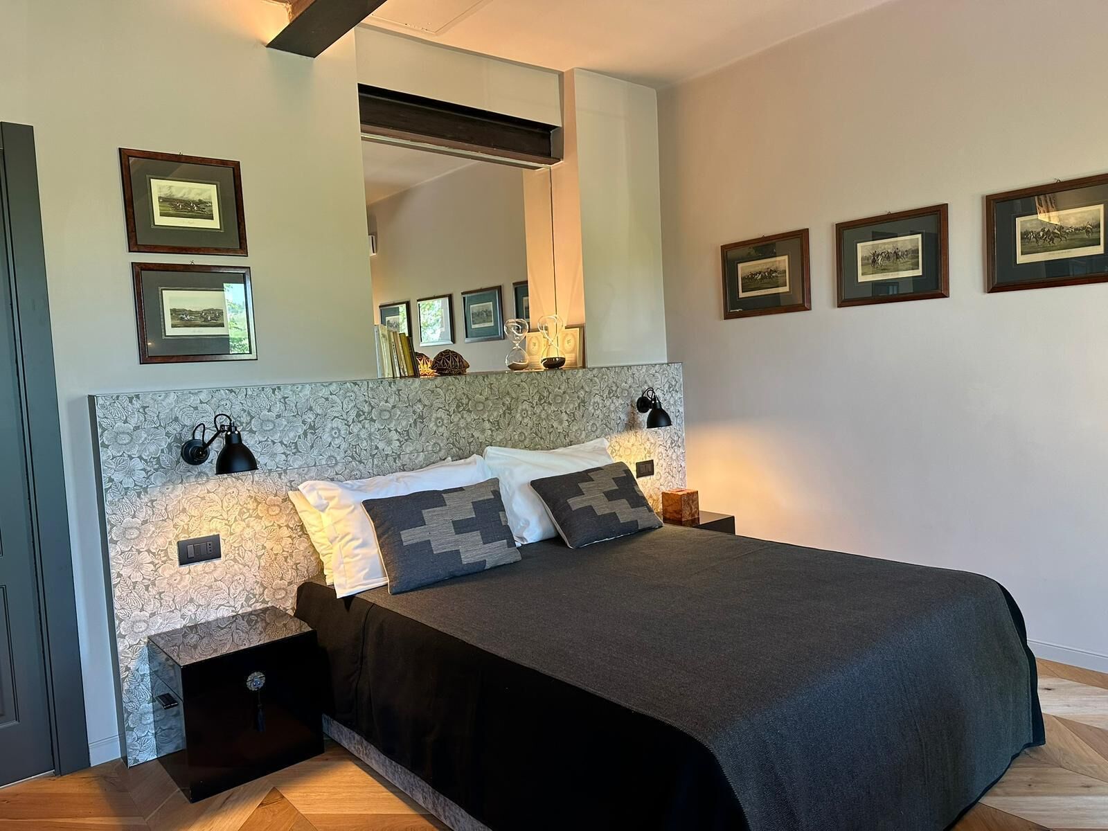 A bedroom with a large bed, a headboard with a floral pattern, bedside lamps, and framed pictures on the wall.