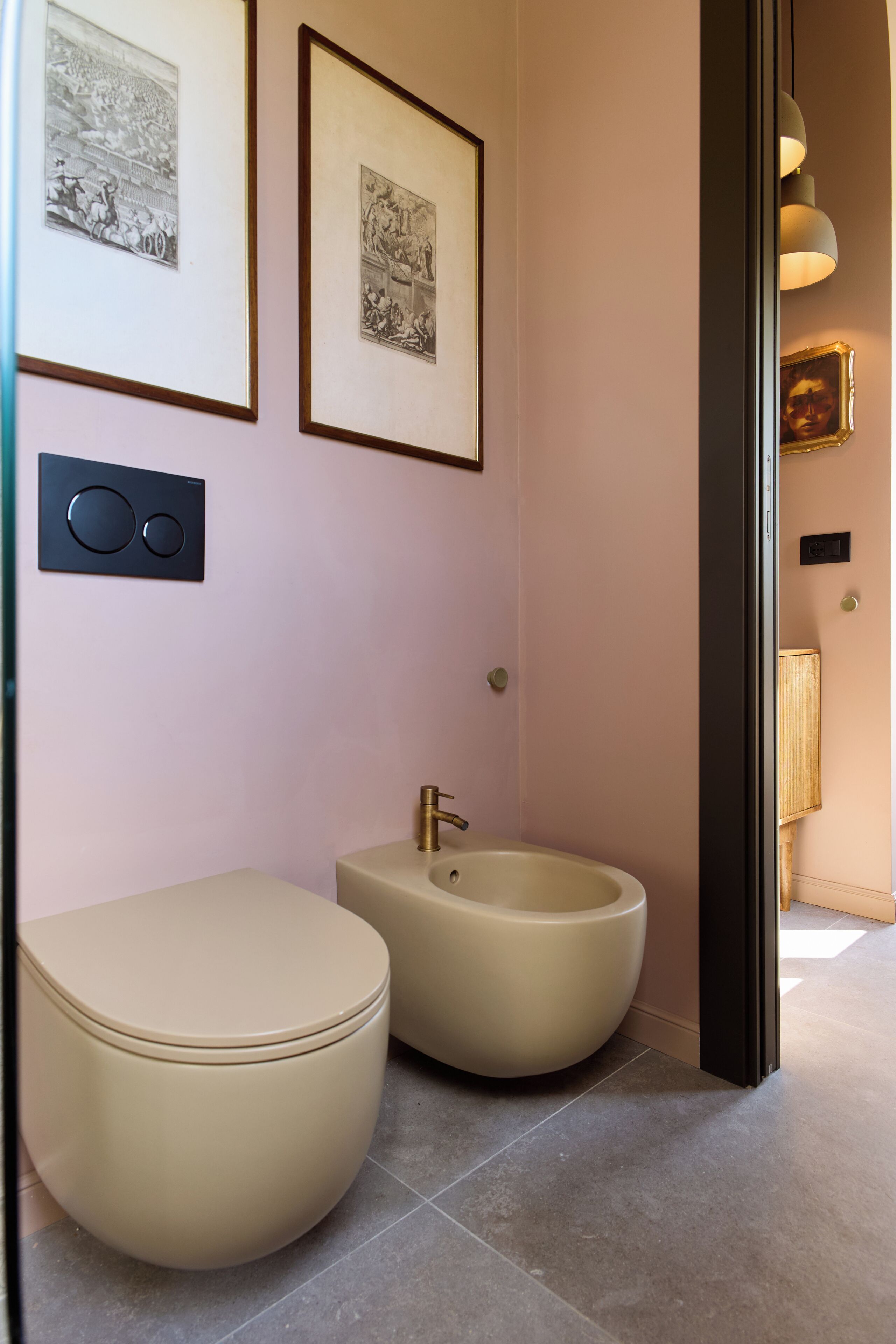 Un bagno con due servizi igienici, un lavabo, quadri appesi alle pareti e una lampada moderna.