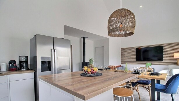 Una cucina moderna con isola in legno, elettrodomestici in acciaio inossidabile e zona pranzo con sedie in vimini e una televisione a schermo piatto.