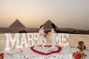 A couple in front of a large illuminated sign with the word 'MARRIAGE' and a pyramid in the background. - Cacillion Pyramids View (Giza)