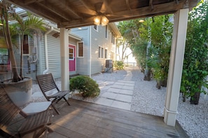 Uma área externa coberta com um deck de madeira, um banco e um caminho que leva a uma casa com porta vermelha.