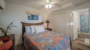Ein Schlafzimmer mit Bett, Deckenventilator, Fenster mit Blick und einer Tür, sowie einer Wand mit Muster.