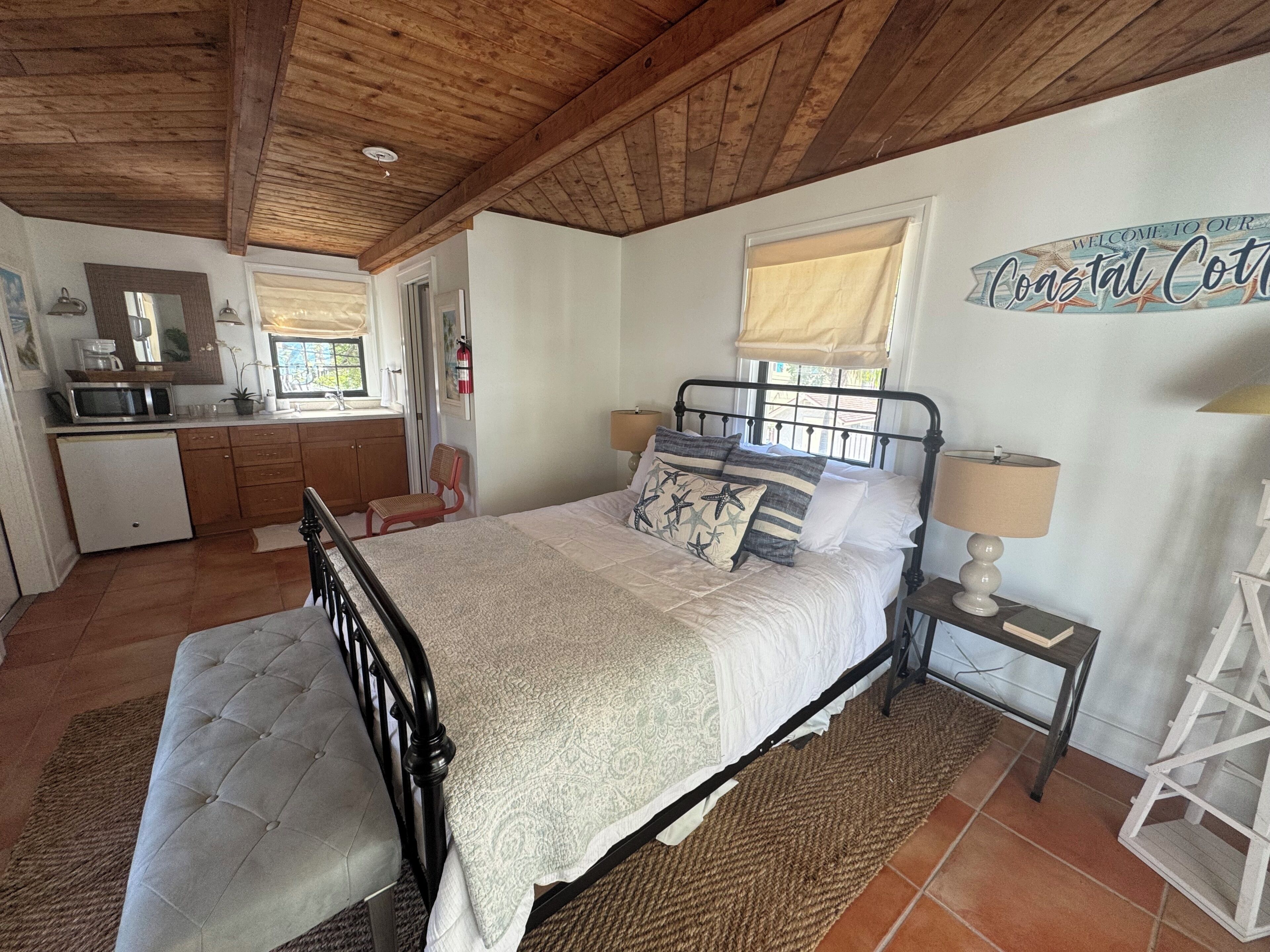 Een slaapkamer met een bed, nachtkastje en uitzicht op de keuken.