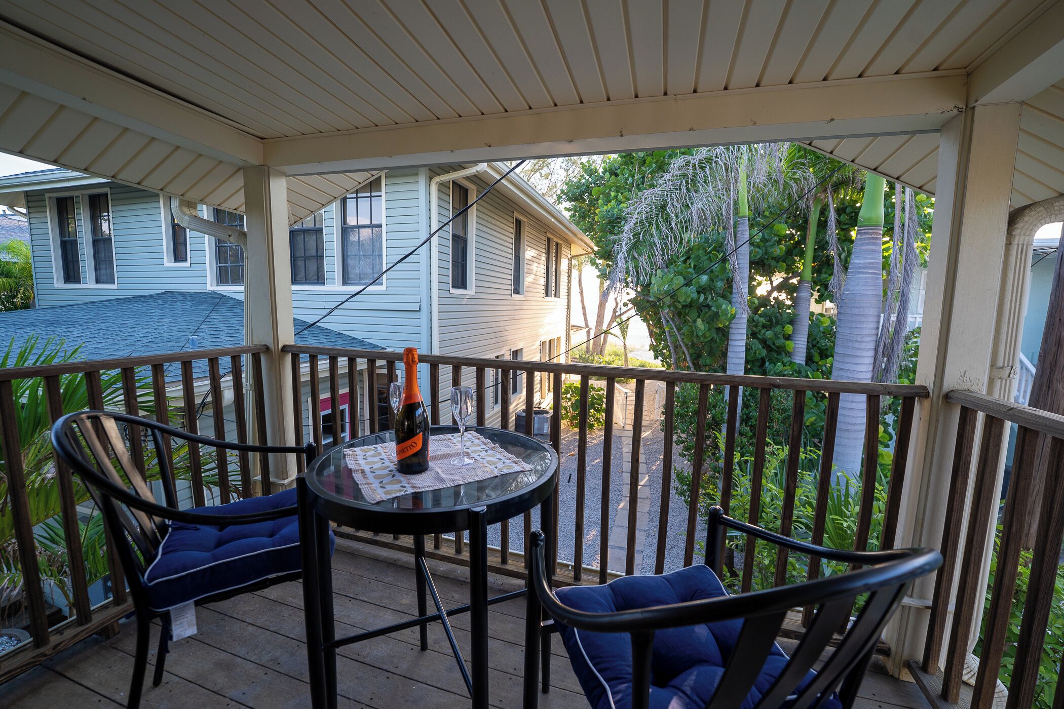 A covered outdoor seating area with a table and two chairs, a bottle, and a glass on the table.