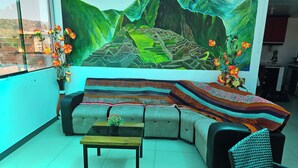 Ein Wohnzimmer mit einer Couch, einem Couchtisch, einer gemusterten Decke und einer großflächigen Wandmalerei einer Berglandschaft.