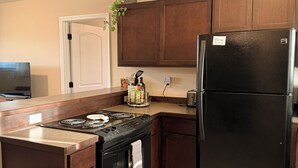 A kitchen with wooden cabinets, a black refrigerator, a stove, and a trash bin. - Bozeman Getaway Guesthouse - Suite C (Bozeman)