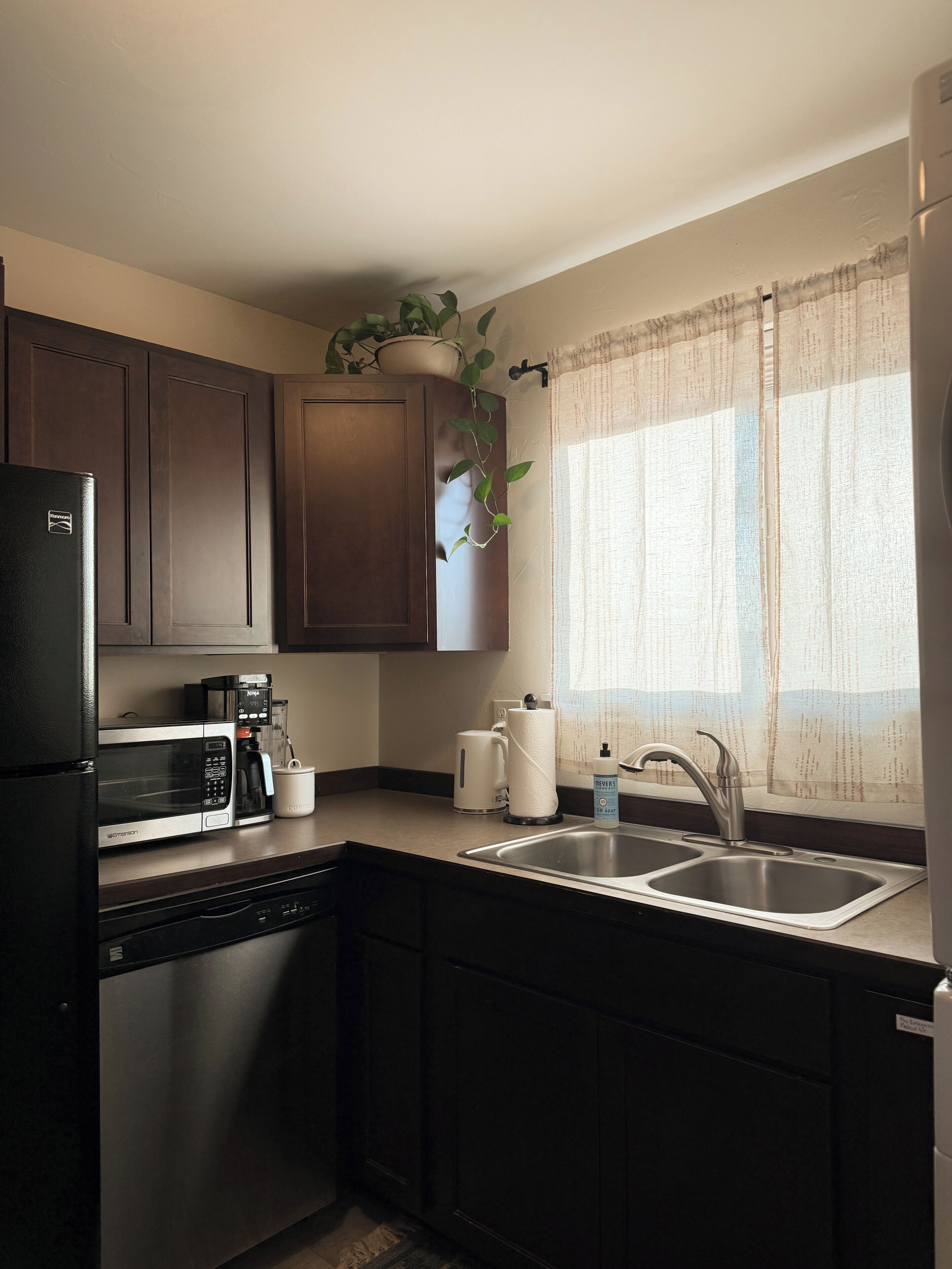 A kitchen with a refrigerator, microwave, coffee maker, and a sink.