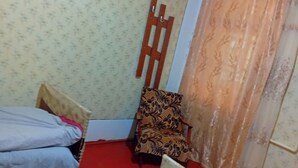 A room with a bed, a chair, a wooden ladder, and a window with curtains.