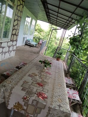 Un balcon abrité, avec une table recouverte d’une nappe et agrémentée de fleurs, une chaise et un pot de fleurs.