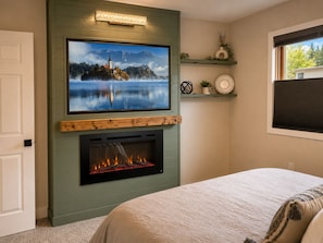 A bedroom with a fireplace, a television mounted above it, and a bed with a white comforter. - River View Chalet -  Fall colors, Flyfishing, close to hunting areas (Fraser)