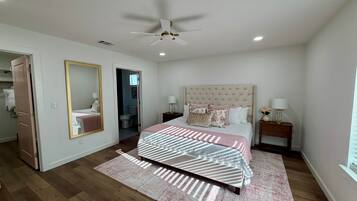 A bedroom with a bed, a ceiling fan, a nightstand, a mirror, and a door leading to another room.