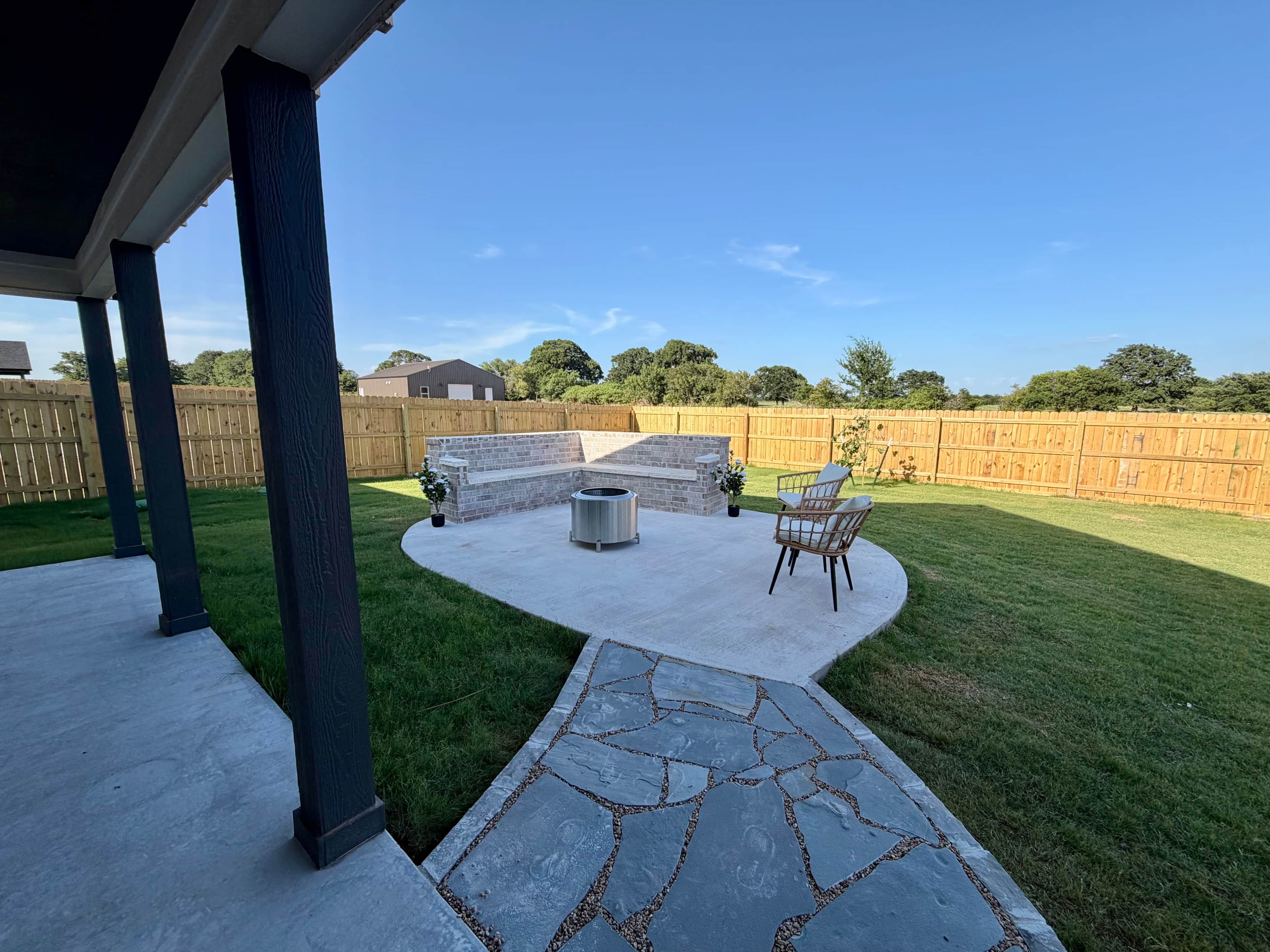 A backyard with a stone patio, a fire pit, and outdoor furniture.