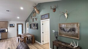 A dining area with a wooden table and benches, a kitchen with wooden cabinets, and a living room with a door and a framed picture on the wall. - Hunter's Lodge by WinStar - King Bed (Love County)