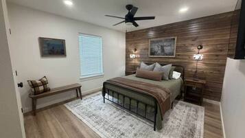 A bedroom with a bed, a bench, a ceiling fan, and wall-mounted lights.