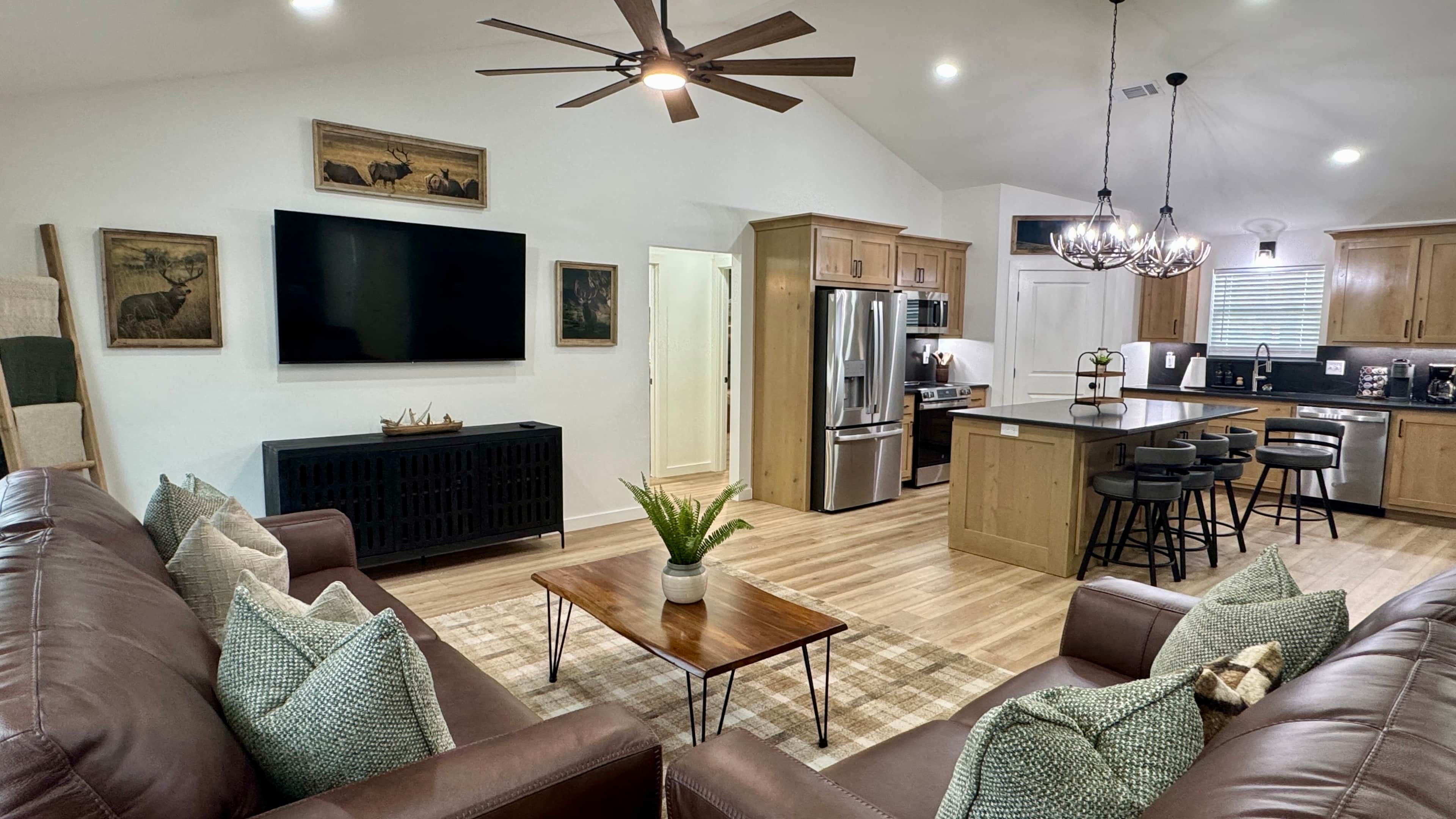 A modern living room with a brown leather sofa, a flat-screen TV, and a ceiling fan.
