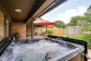 A hot tub under a covered patio with a brick wall, a red umbrella, and a wooden fence in the background. - Cheerful Oasis w/ Private Hot Tub, Yard, & Big Rooms (Fort Worth)