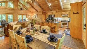 L’intérieur d’un chalet en bois comprend un coin repas, une cuisine et un grand lustre.
